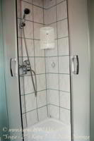 Vonios kambaryje pusapvalė dušo kabina su  paaukštintu padėklu.